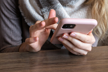 Woman with a finger tattoo and blonde hair scrolling on her pink smartphone rapidly in a cafe, February 2021.