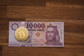 Hungarian forint 10000 forint banknote Saint István King. Brown wooden table. Next to it is a gold bitcoin digital cryptocurrency coin. Bank image and photo.