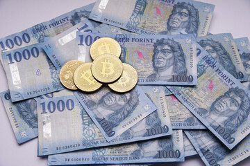 Hungarian banknotes and bitcoin (BTC) digital cryptocurrency coins on a blue background from 1000 HUF paper money.
