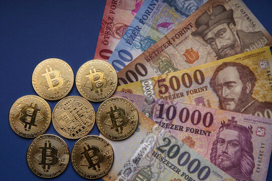Several Hungarian forint paper money denominations with a gold bitcoin digital cryptocurrency coin on a blue background. Bank image and photo.