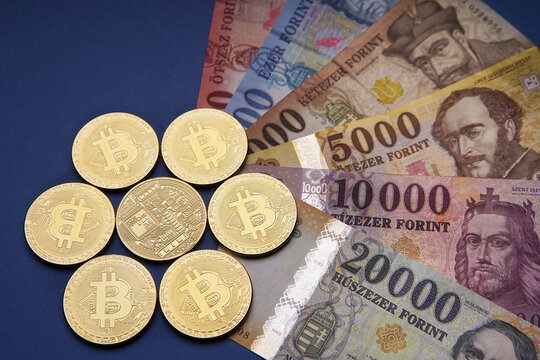 Several Hungarian forint paper money denominations with a gold bitcoin digital cryptocurrency coin on a blue background. Bank image and photo.