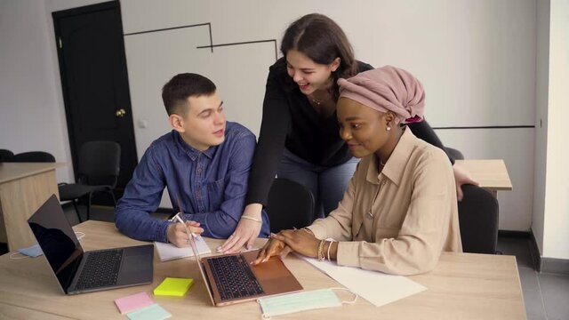 Multiethnic students and teacher study foreign languages together in class. Studing with laptop and medical mask. Black handsome girl student study with white people together