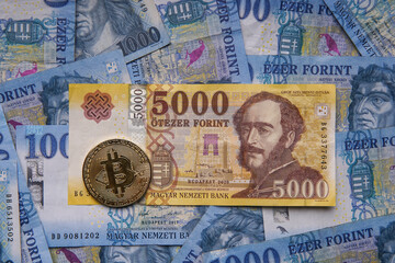 Hungarian banknotes and bitcoin (BTC) digital cryptocurrency coins on a blue background from 1000 HUF paper money.