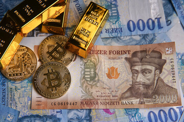Various Hungarian banknotes, gold bars and bitcoin (BTC) digital cryptocurrency coins blue background from 1000 forint paper money.
