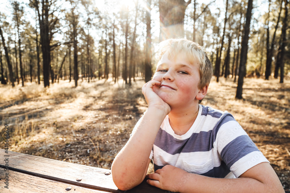 Wall mural happy preteen boy relaxing on park bench in beautiful bush setting