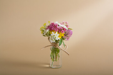 Miniature glass bottle with wildflowers on a beige background for congratulations on March 8, Easter, Mother's Day