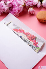 Naklejka premium white envelope with cash around roses and macaroons against pink background. life style concept