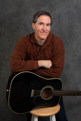 male musician with arms crossed leaning on guitar that is laying on its side