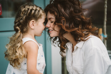 Portrait of little daughter kissing her beautiful happy mother - obrazy, fototapety, plakaty