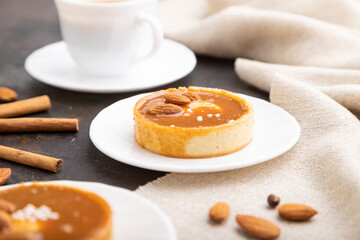 Sweet tartlets with almonds and caramel cream with cup of coffee on a black concrete background. Side view, selective focus.