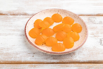 Jelly pumpkin candies on white wooden background, side view.
