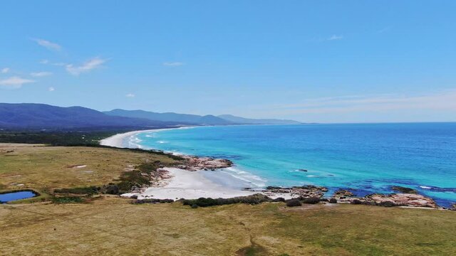 Stunning high angle aerial panoramic drone footage of Denison Beach just north of the village of Bicheno on the east coast of Tasmania, Australia on a sunny day. Rocks in the foreground.