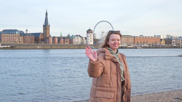 [4k] woman in winter coat waving at camera in front of river rhein and old town of Düsseldorf, Germany