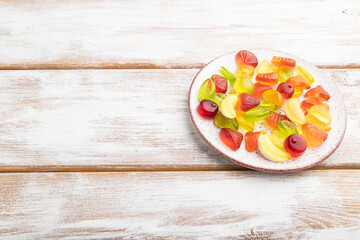 Various fruit candies on plate on white wooden background. copy space, side view.