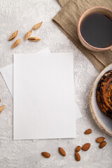 White paper invitation card, mockup with almonds, bun, cup of coffee, linen textile on gray concrete background. flat lay, copy space.