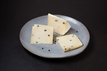 Traditional Italian Caciotta cheese with black pepper on grey plate, close-up. Dark background, selective focus