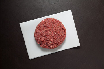 Juicy homemade hamburger, close-up. Raw minced meat on a dark textured background, top view
