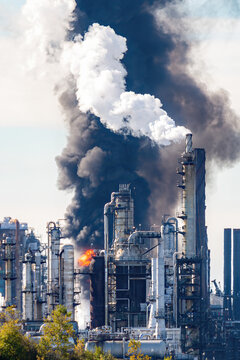 Fire And Black Smoke At An Oil Refinery After An Explosion. Towers Visible In Front Of Smoke And Flame. Scene Slightly Blurred Due To Volatile Air.