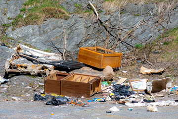 A collection of garbage at the bottom of a rock cliff. Included is broken furniture, plastic bags...