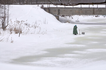 Obraz premium A fisherman speaks on the phone on a frozen river under a bridge.