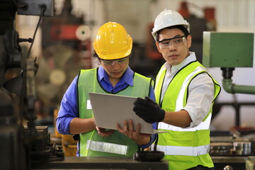 Asian engineering manager and mechanic worker in safety hard hat and reflective cloth using lathe...