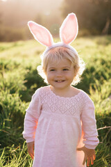 Happy and cute baby girl wear rabbit ears. The girl has blonde curly hair and a pink dress. Easter concept. 