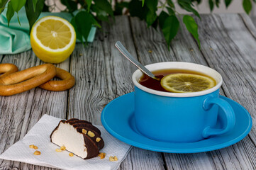 A cup of black tea with lemon stands on a wooden table.