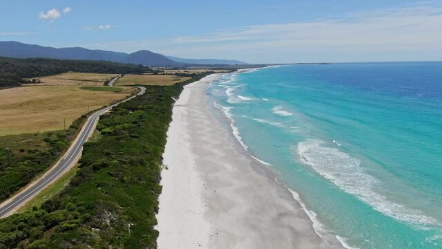 Stunning high angle aerial panoramic drone footage of Denison Beach and the A3 Tasman Highway just north of the village of Bicheno on the east coast of Tasmania, Australia on a sunny day.