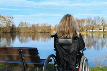 Fototapeta premium Concept of disabled person. A woman in a wheelchair outside in the nature in front of a lake. 