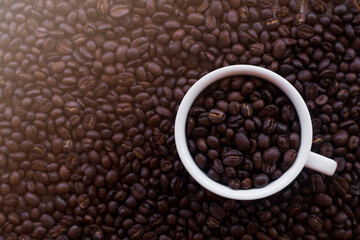 Coffee cup with roasted beans on coffee beans background. Top view with copy space. Top view coffee beans background with white coffee cup
