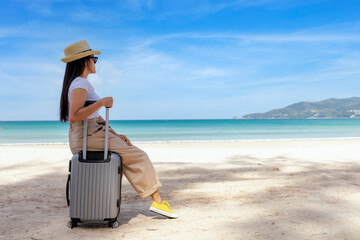 Fototapeta na wymiar Young happy woman sit on travel suitcase on the beach in summer. Travel woman looks at the sea. Women sitting and relax with beach and sky background. Holiday summer vacation