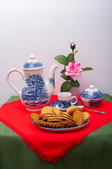 breakfast with chocolate cookies, cup of coffee, coffee or tea pot and vase with pink flowers.

