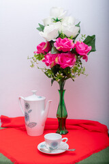 Breakfast service with a cup of coffee, coffee maker, kettle and vase with pink flowers.
