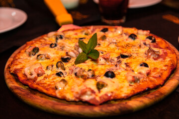 An appetizing pizza with seafood and cheese lies on a wooden plate on the table. With a pizza knife.