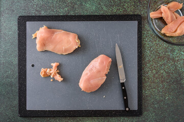 Fresh raw chicken breast on cutting board being cut into chicken strips, beginning dinner preparation
