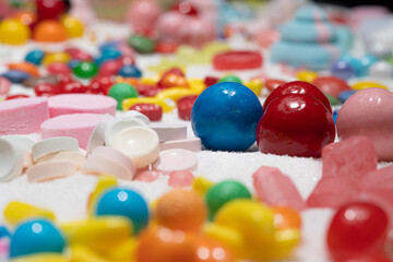 Candy in variety of colour, shape, size and flavours mixed on the table with real white sugar. Macro. Shallow depth of field. International Candy Day background. Sweet stock of snack.