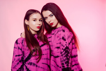 2 girls in the same things with bright makeup. Brunette girls, sisters, girlfriends, twins. Women's power, March 8, Women's Day. Clothing store for teens. Pink color in clothes, pink background.