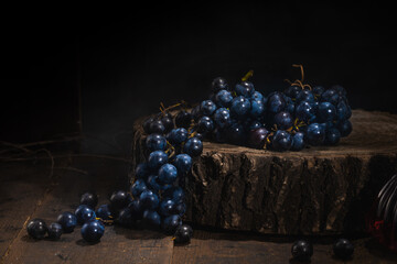 Multiple whole bunches of grapes and grape granules placed on a wooden plate against a dark...