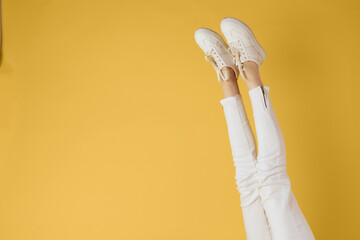 Female legs white jeans sneakers fashion yellow background view