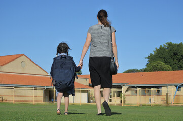 Rear view of a mother and young daughter holding hands walking together to school.