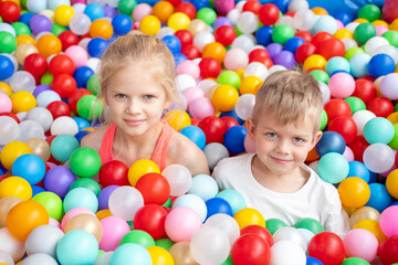 Fototapeta na wymiar Portrait close up Smiling blonde little boy and girl lying on multi colored plastic balls in big dry paddling pool in playing centre. Having fun in playroom Leisure Activity.