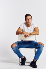 A man in jeans sits on a chair backwards and and ripped jeans T-shirt front view