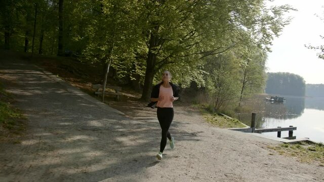 Woman running next to lake and woods on sunny day