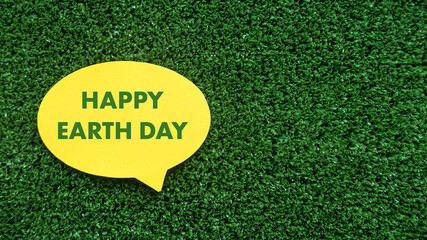 A yellow speech bubble with text of Happy Earth Day on green grass background with copy space.