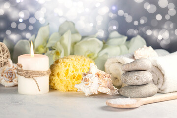 Massage stones, natural sea sponge, seashell, burning candles, rolled towels, sea salt, orchid flowers, abstract lights. Spa resort therapy composition