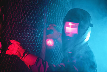 Welder in the neon lights in the welding helmet.