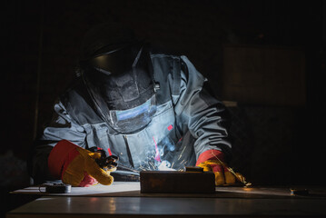 Welder is welding a metal pipe on the workbench.