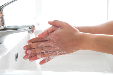 Hands of woman wash their hands in a sink with foam to wash the skin and water flows through the hands. Concept of health, cleaning and preventing germs and coronavirus from contacting hands