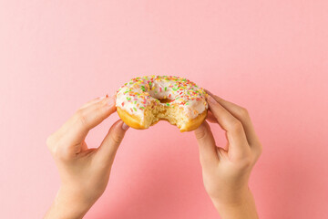 A bitten glazed doughnut in the hands of a girl on a pink background.