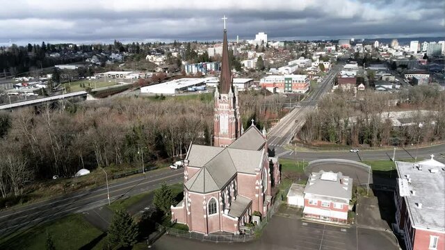 Sun shines on the Holy Rosary Catholic Church, storm clouds in the background, aerial orbit